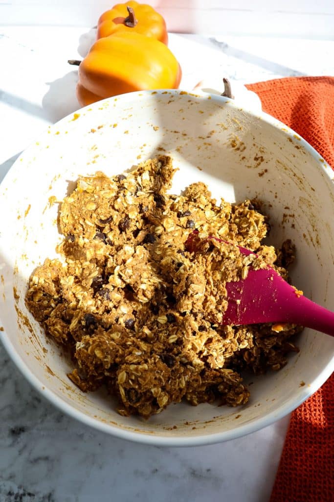Ingredients for pumpkin protein balls being mixed together in a mixing bowl with rubber scraper.