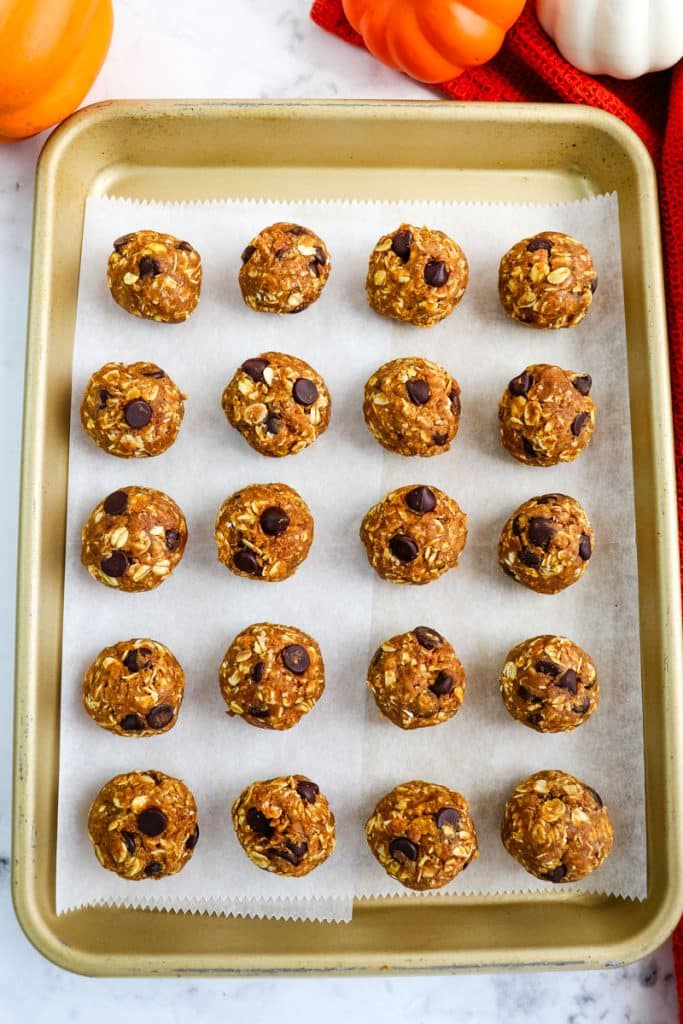 Pumpkin chocolate chip protein balls rolled and lined up on a sheet pan lined with parchment paper.