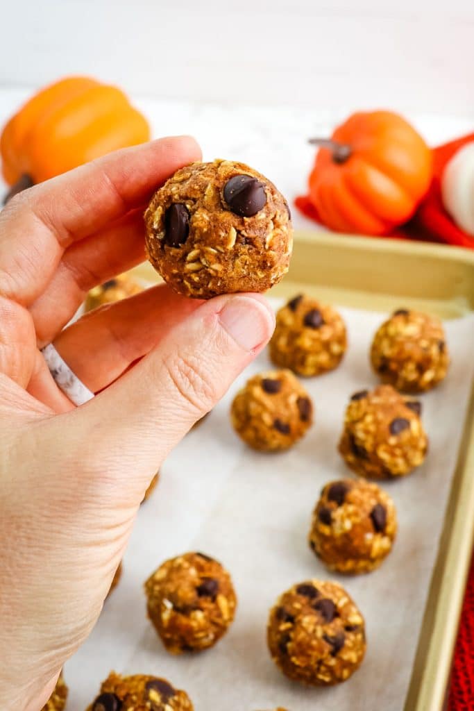 Pumpkin protein ball held in hand with other balls in the background.