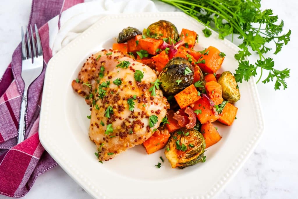 Maple glazed chicken thigh with side of sweet potatoes, roasted brussels sprouts topped with parsley.