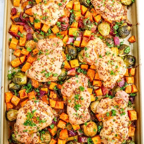 Roasted maple dijon chicken on top of sweet potatoes, brussels sprouts and red onion, all on a sheet pan.