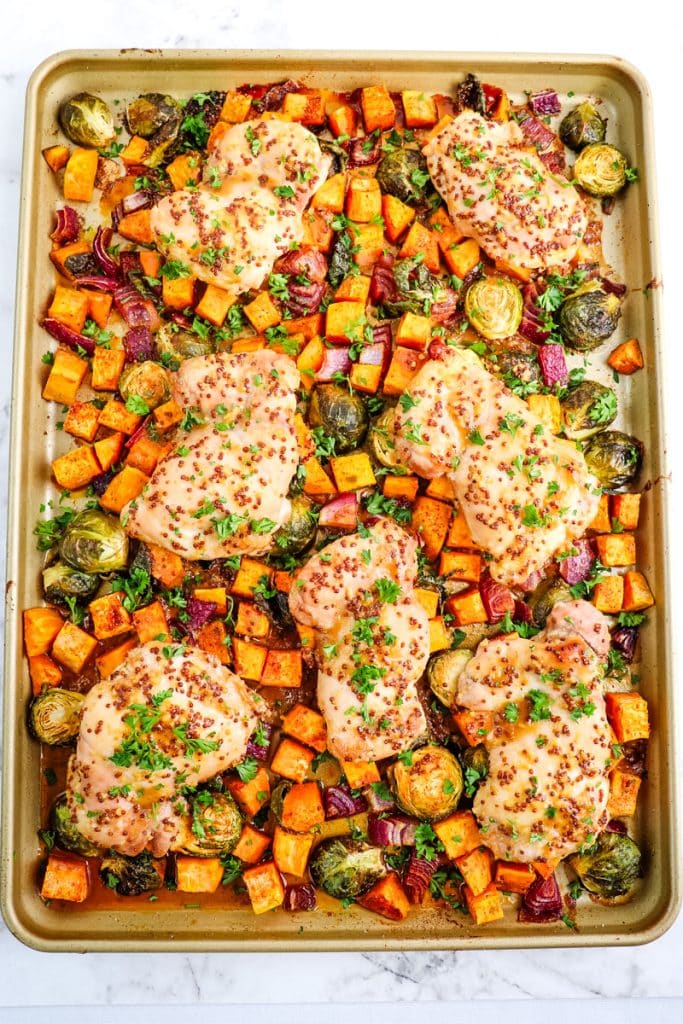 Roasted maple dijon chicken on top of sweet potatoes, brussels sprouts and red onion, all on a sheet pan.