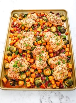 Sheet pan maple dijon chicken thighs with sweet potatoes and brussels sprouts all topped with chopped parsley.
