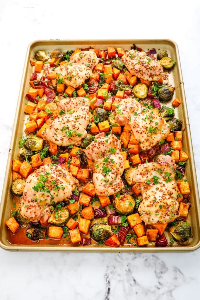 Sheet pan maple dijon chicken thighs with sweet potatoes and brussels sprouts all topped with chopped parsley.