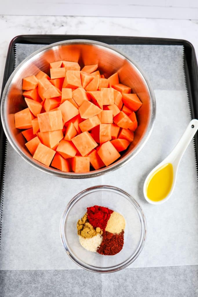 Bowl of peeled and cubed sweet potatoes, tablespoon of olive oil and small bowl of spices.