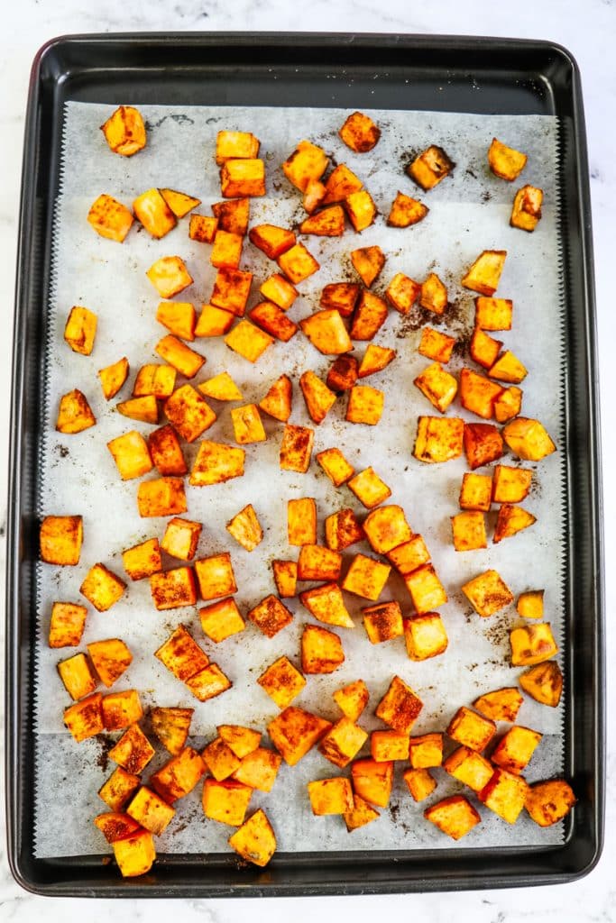 Seasoned and roasted sweet potatoes on a sheet pan.