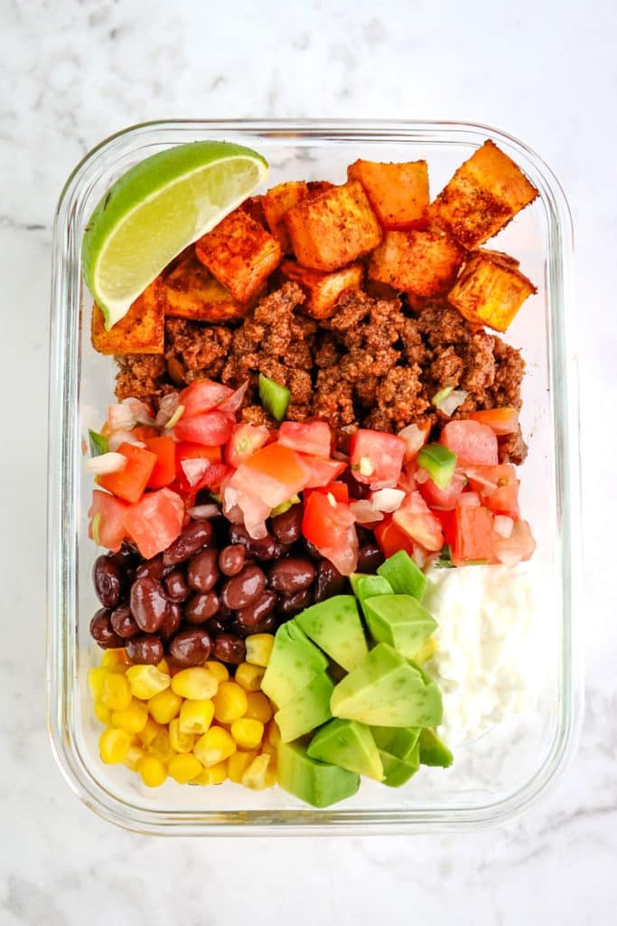 Ground beef taco bowl in a glass meal prep container with sweet potato, salsa, beans, corn and cottage cheese.