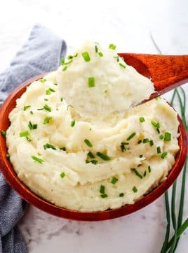 Boursin mashed potatoes in bowl topped with chives with spoon taking out a scoop.
