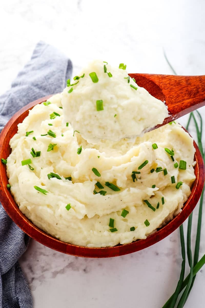 Boursin mashed potatoes in bowl topped with chives with spoon taking out a scoop.