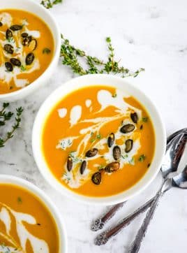 Bowl of carrot and butternut squash soup with spoons and thyme sprigs on the side.