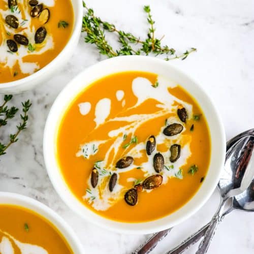 Bowl of carrot and butternut squash soup with spoons and thyme sprigs on the side.