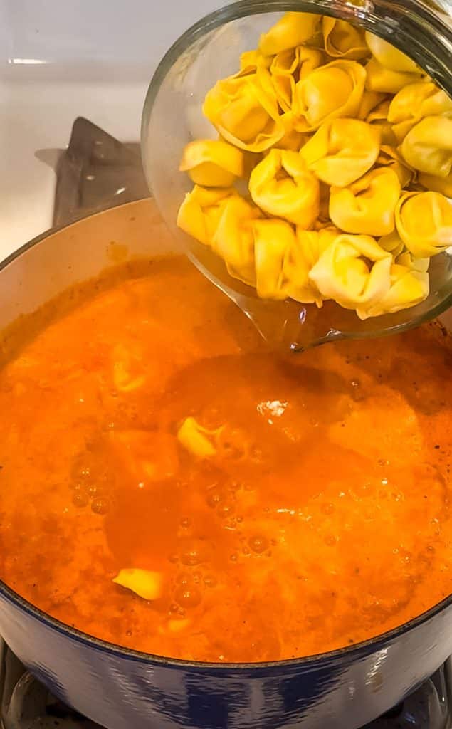 Tortellini being added to the simmering creamy tomato soup.