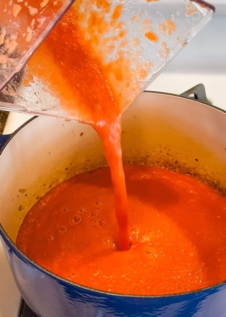Pureed tomatoes, onions and garlic being poured into a soup pot.