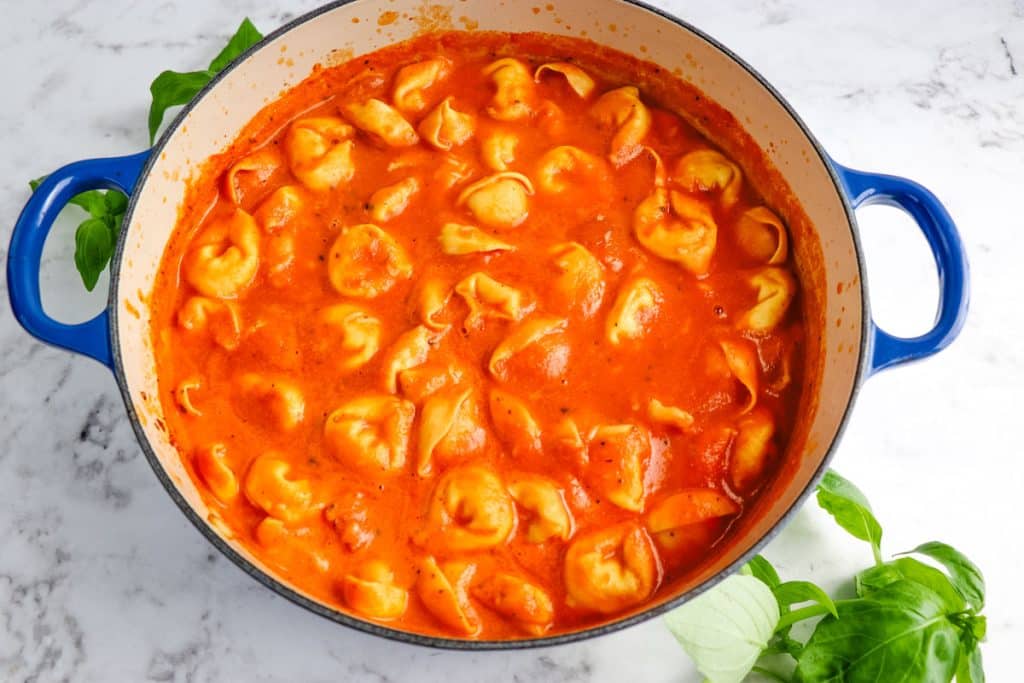 Creamy tomato tortellini soup with fresh basil leaves on the side of the pot of soup.
