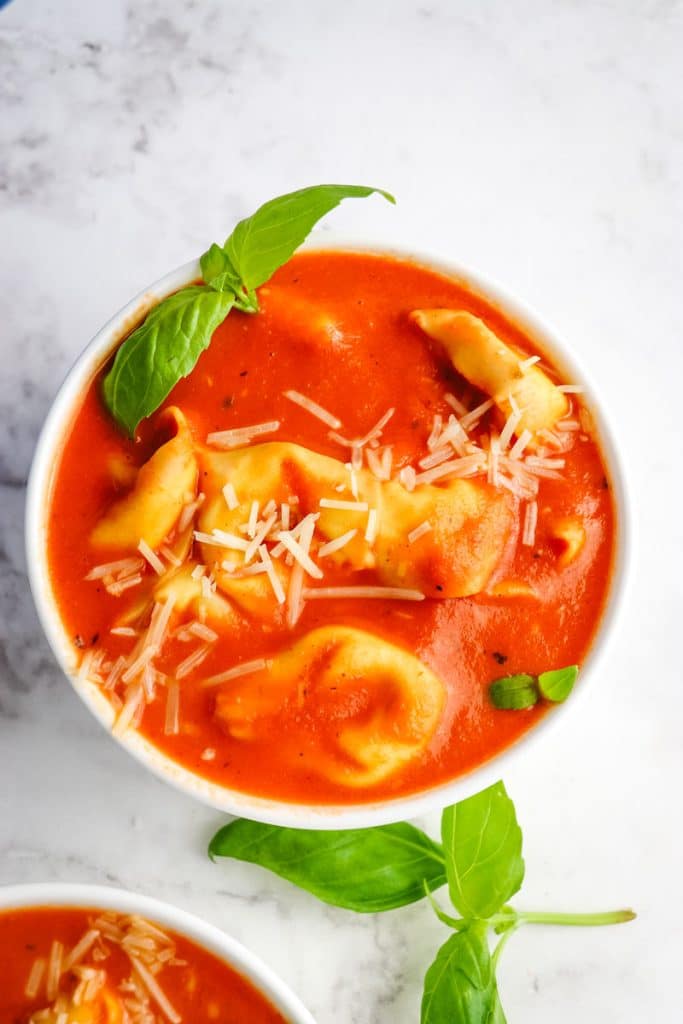 Bowl of creamy tomato and tortellini soup topped with parmesan cheese and basil leaves.