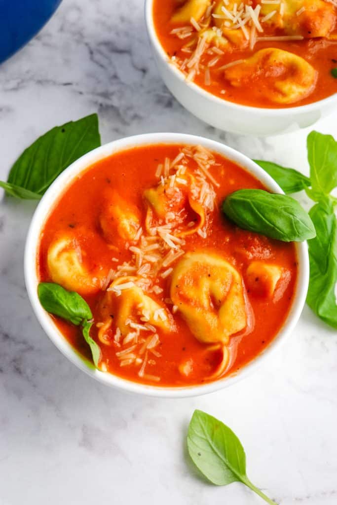 Two bowls of creamy tomato tortellini soup topped with shredded Parmesan cheese and fresh basil leaves.