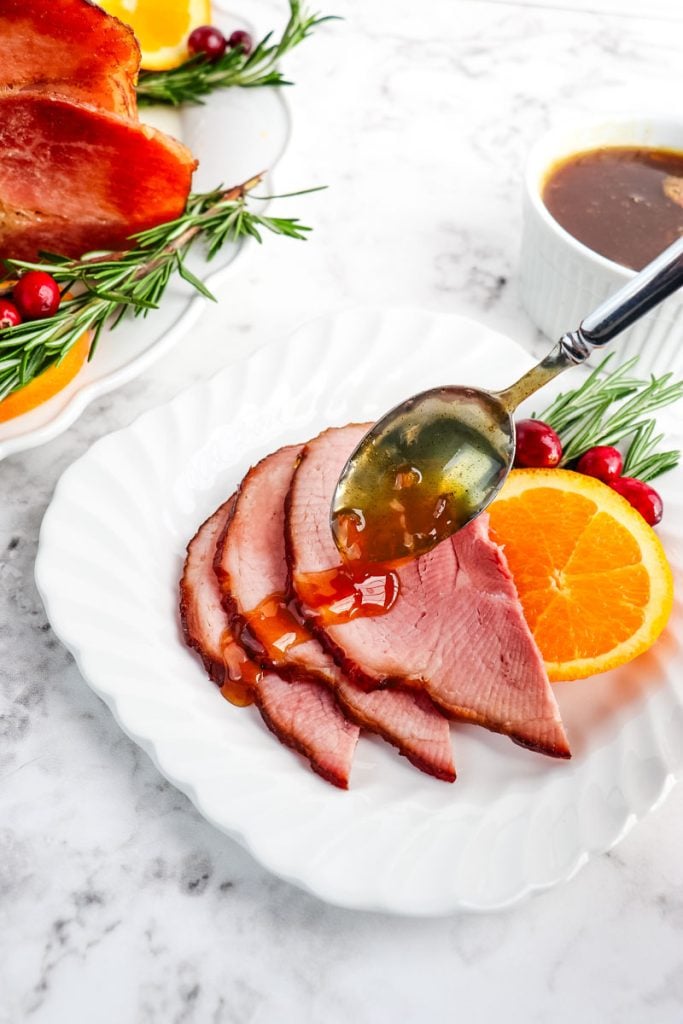 Ham slices on a plate with orange glaze being spooned over the top of the ham.