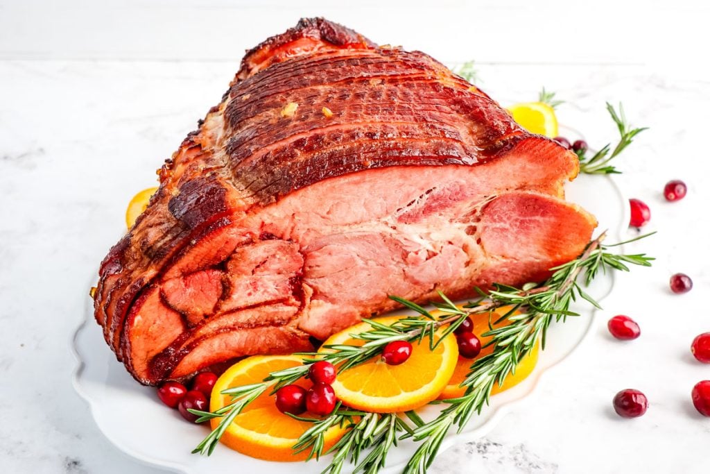 Orange glazed ham garnished with rosemary, fresh cranberries and orange slices.
