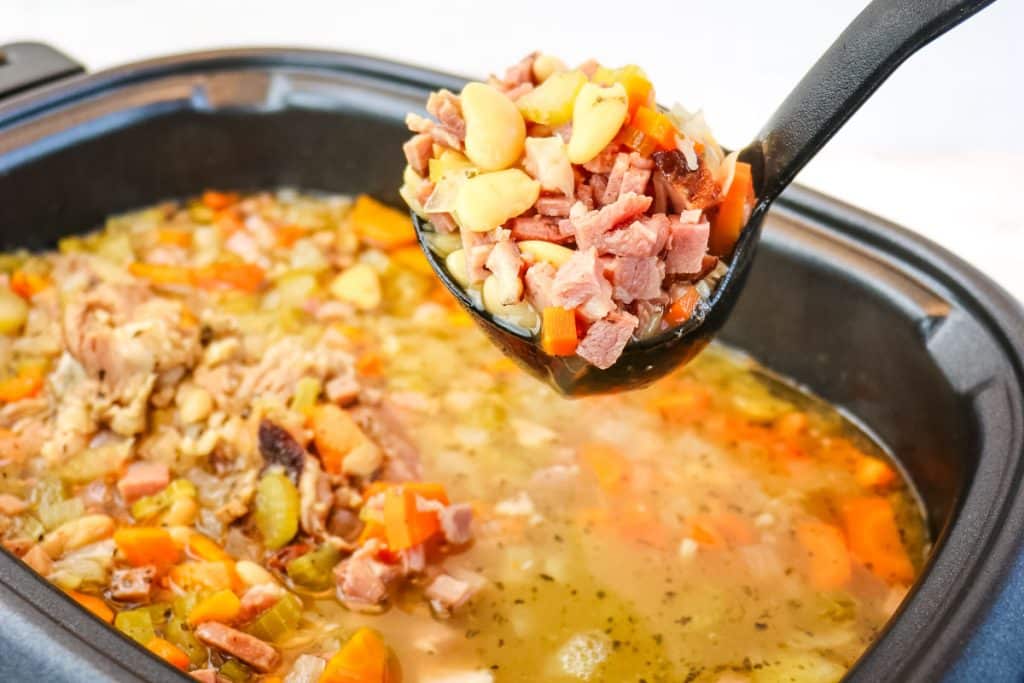 Slow cooker ham and bean soup being ladled out of a slow cooker.