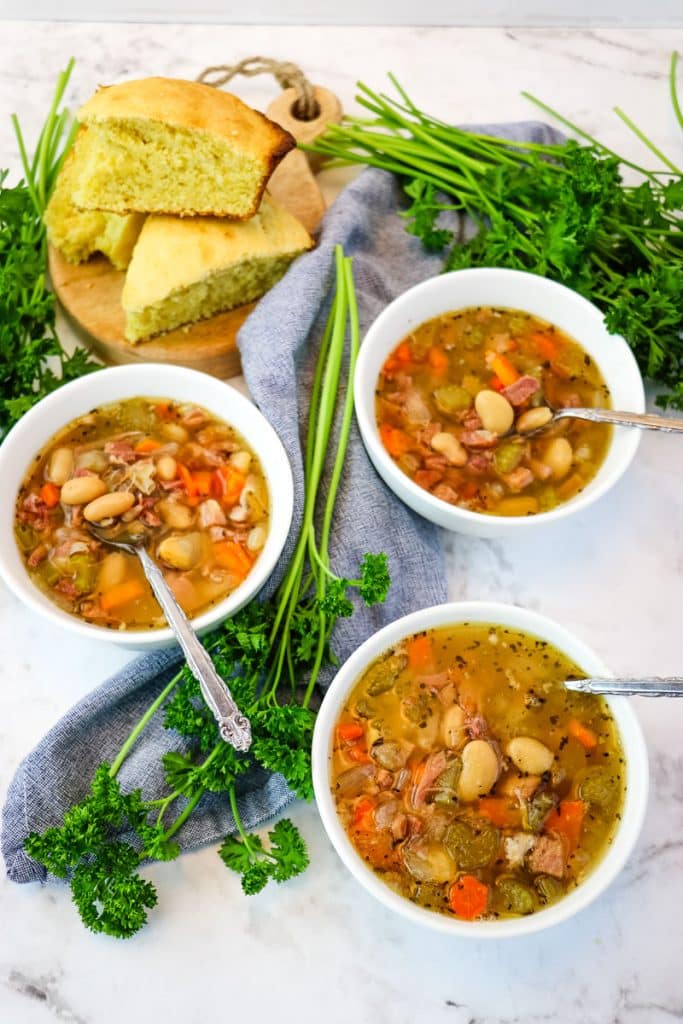 Ham and bean soup in white bowls with corn bread in the background.