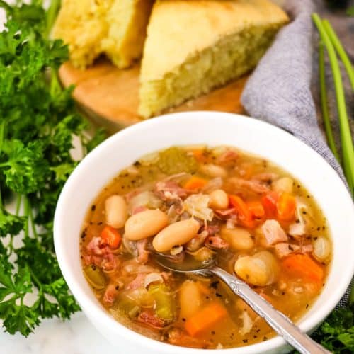 Slow cooker ham and bean soup in a bowl with corn bread in the background.