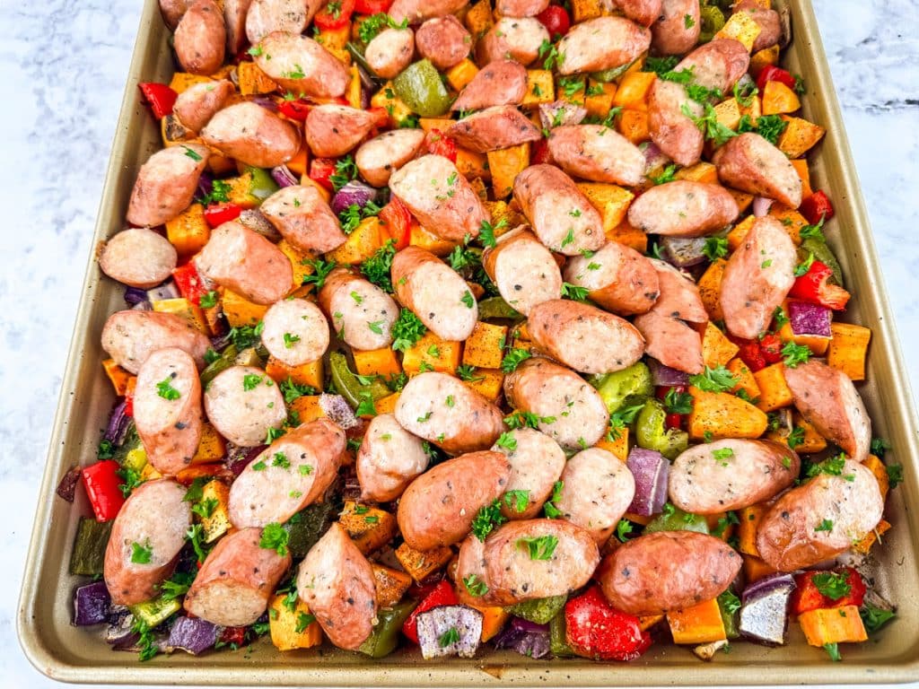 Oven baked sausage and peppers with sweet potatoes on a sheet pan.
