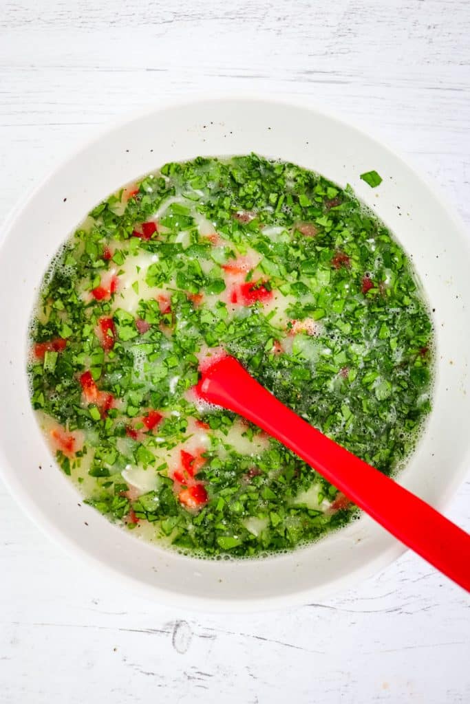 Mixing bowl with egg white ingredients mixed together with spinach and red bell pepper.