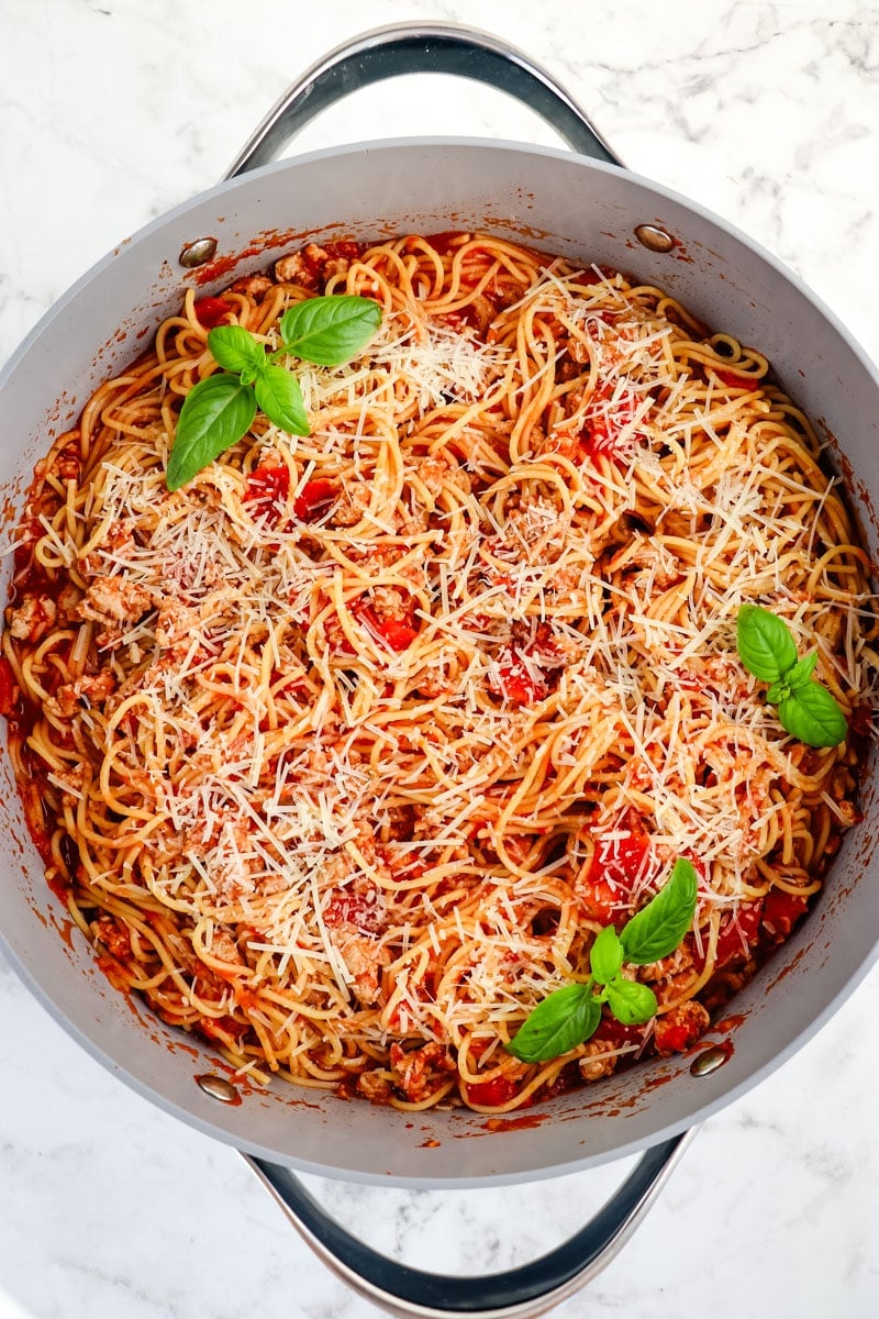 Turkey spaghetti in red sauce in a skillet garnished with fresh basil.
