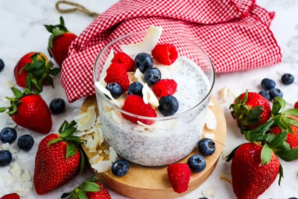 Jar of coconut milk chia pudding topped with fresh berries and sliced coconut.