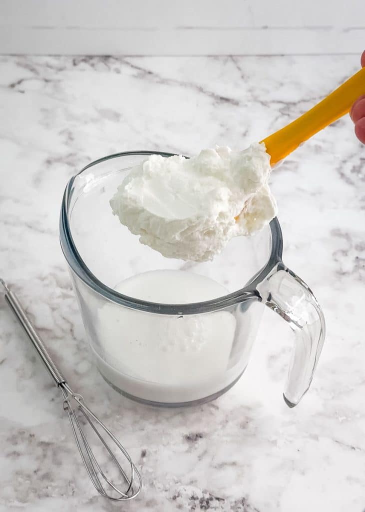 Small mixing bowl with milk and yogurt being added to it, with mini whisk on the side.