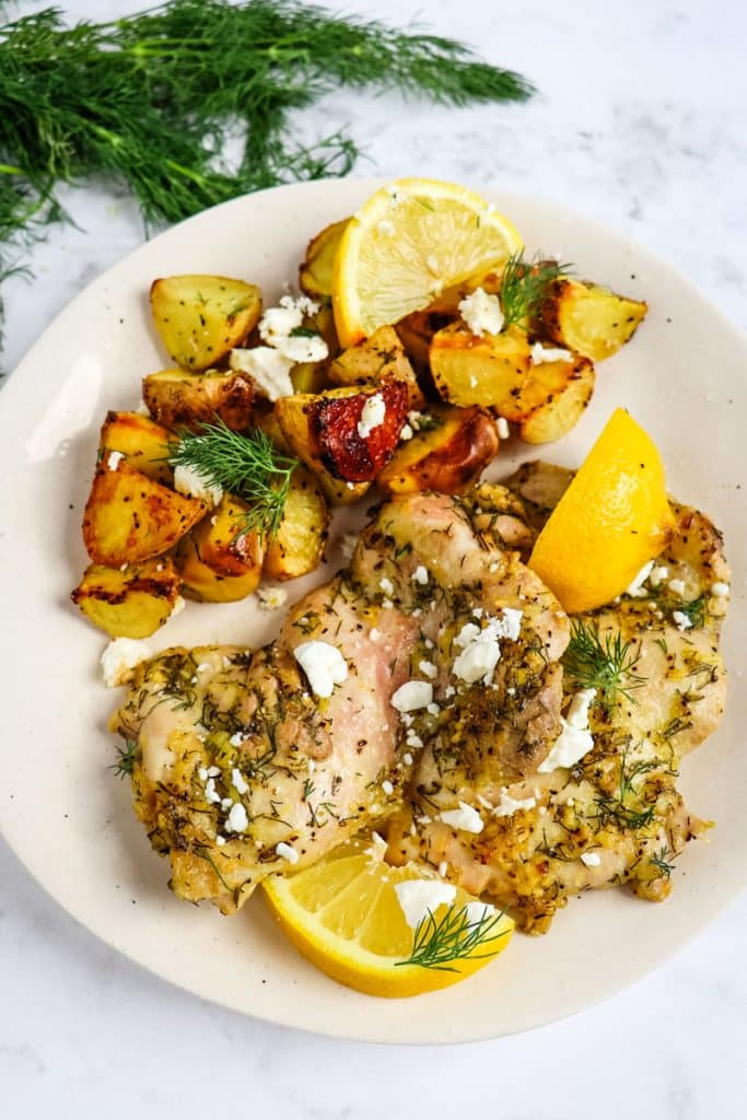 Greek chicken and lemon potatoes on a plate, garnished with lemon slices.