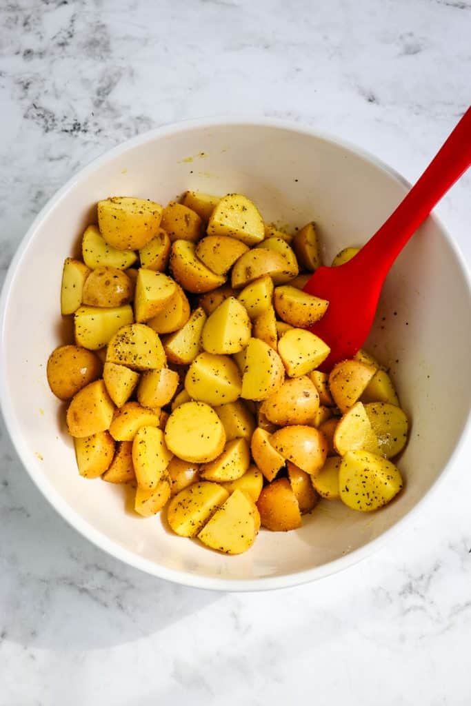 Lemon potatoes cut and in a mixing bowl with lemon pepper seasoning.