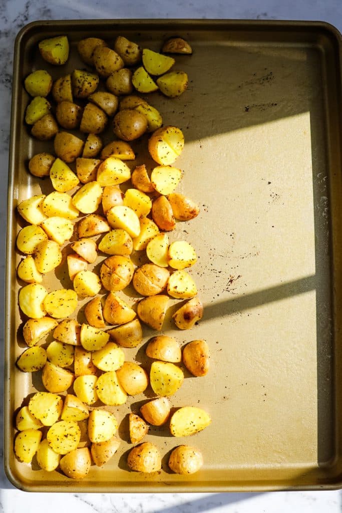 Quartered baby Yukon gold potatoes on a sheet pan ready to go into the oven.