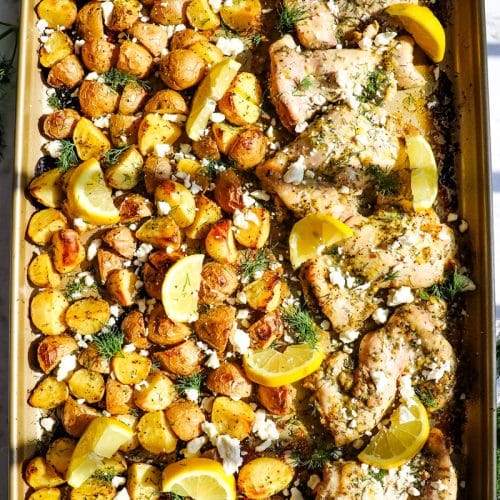 Sheet Pan Greek Chicken and lemon potatoes topped with fresh dill, lemon slices and feta cheese crumbles.