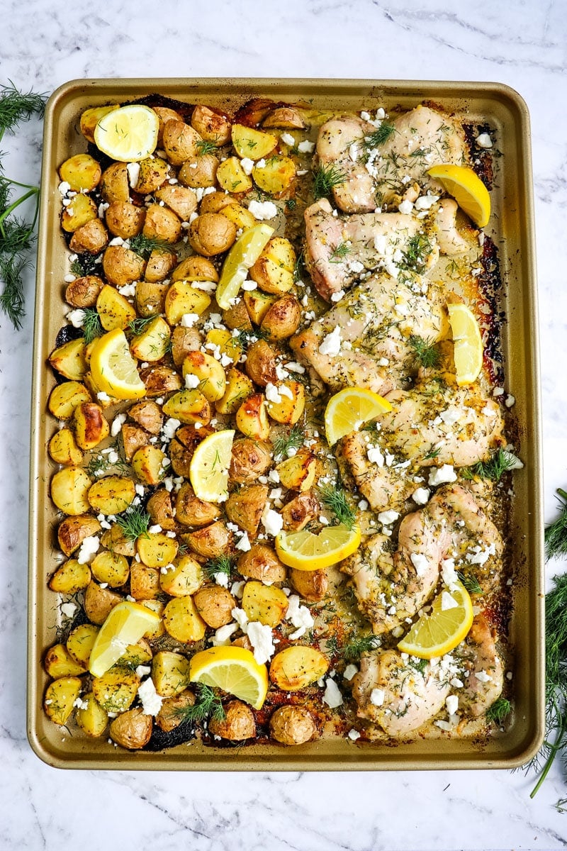 Sheet pan Greek chicken and lemon potatoes topped with lemon slices, feta cheese crumbles and minced dill.
