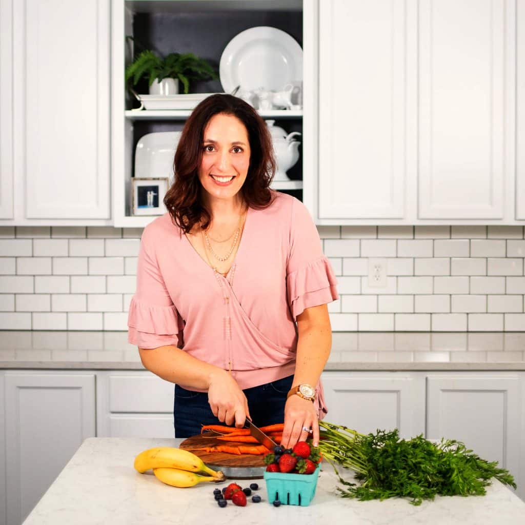 Erin in a kitchen chopping vegetables and fruits.