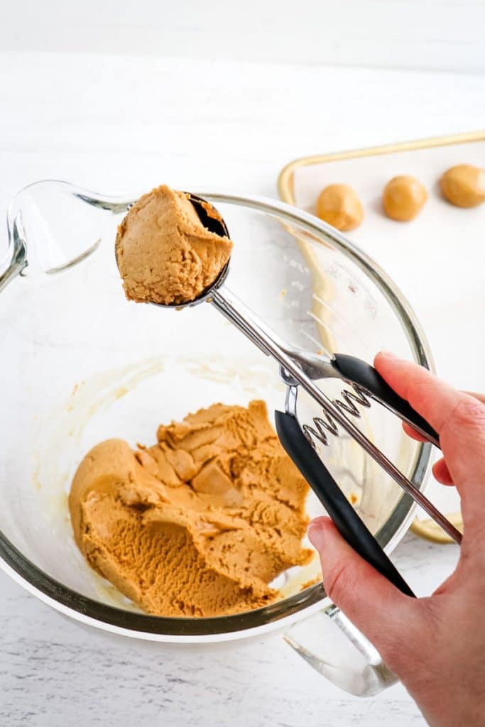 Cooking scoop with peanut butter protein ball batter being scooped out of bowl.
