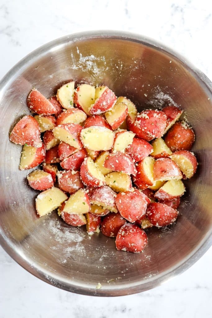 Quartered baby red potatoes in a mixing bowl that have been coated with grated parmesan cheese and ranch seasoning.