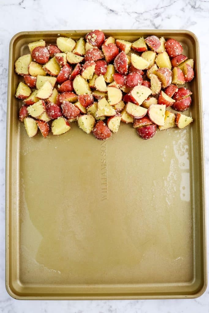 Quartered baby potatoes that have been placed on the top section of a sheet pan.