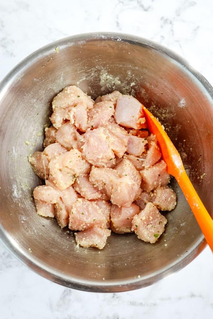 Raw chicken breast meat that has been cut into cubes, and coated with ranch seasoning and grated parmesan cheese.