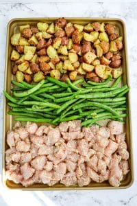 Quartered potatoes, green beans and seasoned chicken breast pieces on a sheet pan ready to roast.