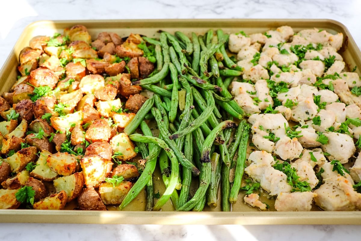 Chicken potatoes and green beans on a sheet pan topped with fresh parsley.