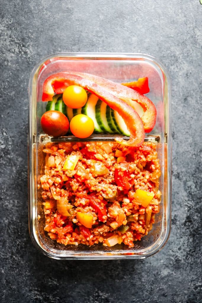 Unstuffed peppers casserole in a meal prep container with fresh vegetables.